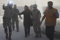 Civil defense members help a woman in a site hit by what activists say was a barrel bomb dropped by forces loyal to Syria's President Bashar al-Assad, at Aleppo's Saif al-Dawla district May 7, 2015. REUTERS/Hosam Katan