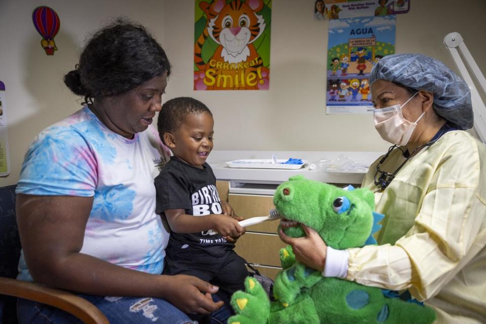 A dental hygienist holds open the mouth of a stuffed animal so a young boy can learn good teeth brushing habits.