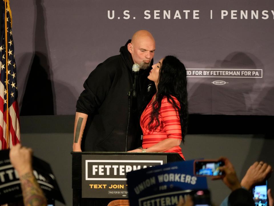 John Fetterman and Gisele Fetterman kiss onstage during a rally