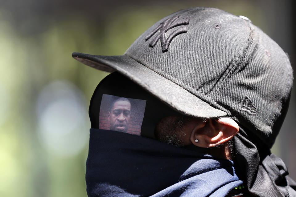 CORRECTS THE DATE OF FLOYD'S DEATH TO MARCH 25 - NOT 29 - A man wears a protective face covering with George Floyd's image on it as he listens to speakers during a Pray & Protest rally and march, Sunday, June 7, 2020, in the Bedford-Stuyvestant neighborhood of the Brooklyn borough of New York. Floyd died May 25 in Minneapolis while in the custody of police officers. His death has sparked hundreds of protests, coming on the heels of the deaths of other black men and women. (AP Photo/Kathy Willens)