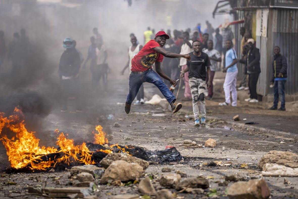 A protester jumps in the air as he throws a rock towards police next to a burning barricade in the Kibera slum of Nairobi, Kenya, Monday, March 20, 2023. (AP Photo/Ben Curtis)
