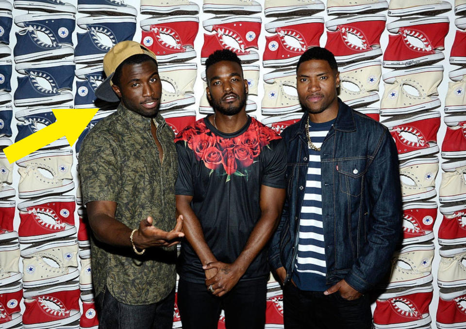 Y'lan Noel standing in front of a backdrop of rows of Converse shoes with two other guys