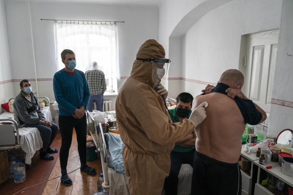 In this photo taken on Friday, May 1, 2020, a doctor, wearing a special suit to protect against coronavirus, checks a patient with coronavirus with a stethoscope during evening examination at a hospital in Pochaiv, Ukraine, Friday. Ukraine's troubled health care system has been overwhelmed by COVID-19, even though it has reported a relatively low number of cases. (AP Photo/Evgeniy Maloletka)