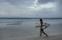 A surfer carries his board on Playa Gaviota Azul as Tropical Storm Zeta approaches Cancun, Mexico, Monday, Oct. 26, 2020. A strengthening Tropical Storm Zeta is expected to become a hurricane Monday as it heads toward the eastern end of Mexico's resort-dotted Yucatan Peninsula and then likely move on for a possible landfall on the central U.S. Gulf Coast at midweek. (AP Photo/Victor Ruiz Garcia)