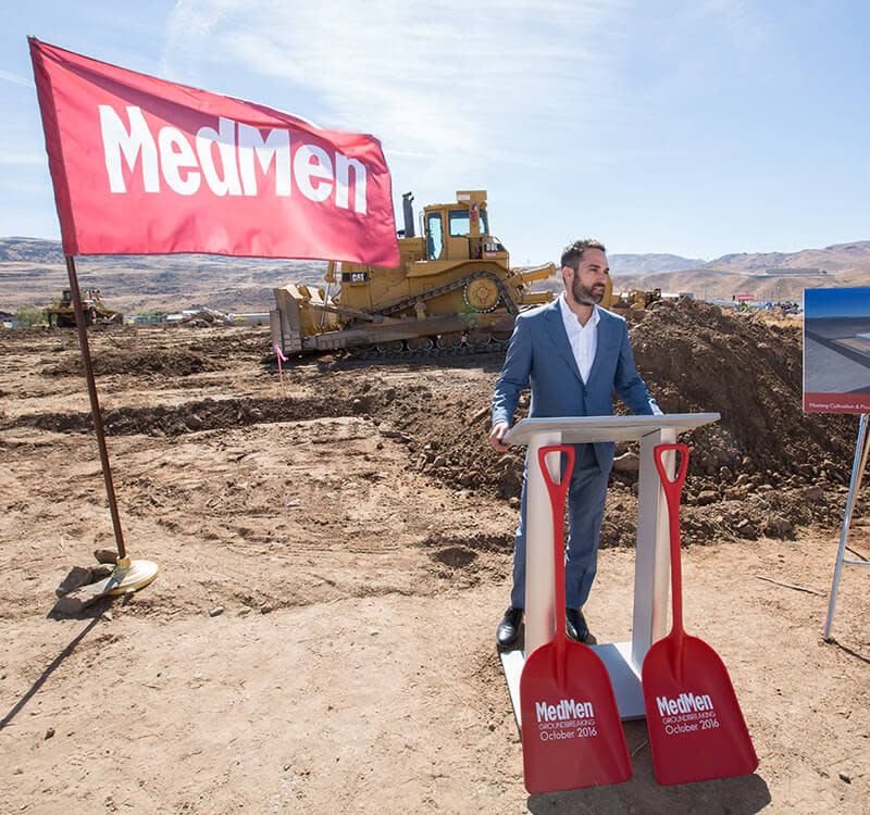 MedMen CEO Adam Bierman speaks at a podium in front of a construction site next to a MedMen flag.