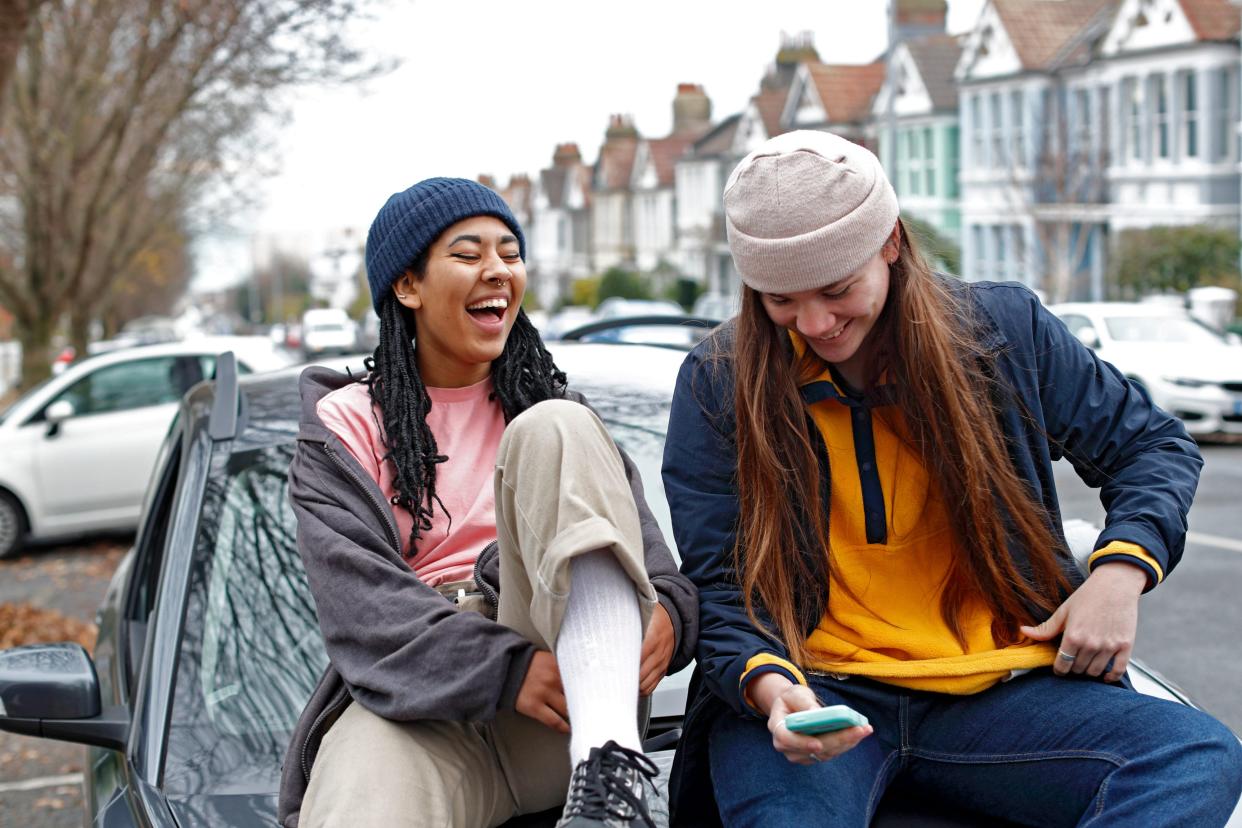 Two women sitting laughing sitting on car