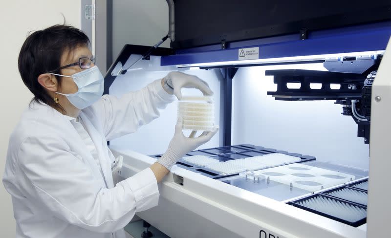 An employee of Swiss biotechnology company Molecular Partners takes samples out of a colony picker robot in a laboratory at the company's headquarters in Schlieren