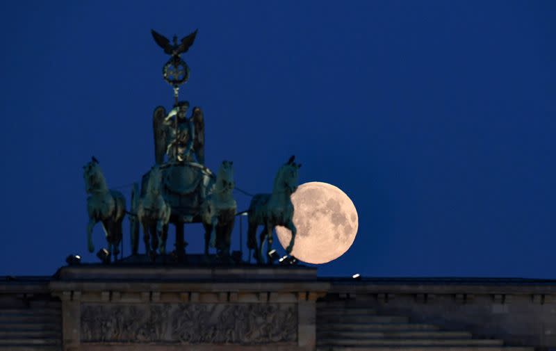 An almost full moon is seen behind the quadriga of Brandenburg Gate in Berlin