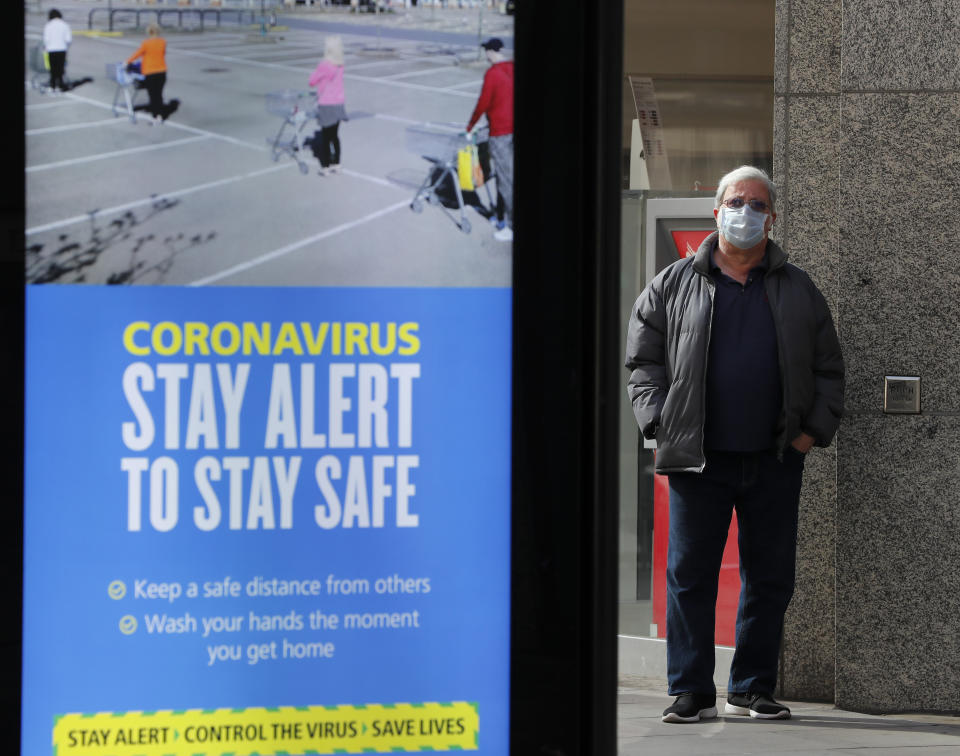 A man wearing a face mask waits on a bus stop next to a government advert with the new theme: 'Stay Alert', in London, Tuesday, May 12, 2020, as the country continues in lockdown. Britain's Prime Minister Boris Johnson announced Sunday that people could return to work if they could not work from home. (AP Photo/Frank Augstein)