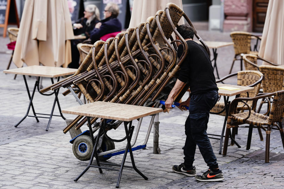 The employee of a pub rolls a stack of chairs onto the market place in Heidelberg, Germany, Saturday, May 15, 2021. After months of lockdown, the Southwest is loosening the reins on Corona rules significantly. From Saturday on, openings in gastronomy, tourism and leisure are possible. (Uwe Anspach/dpa via AP)