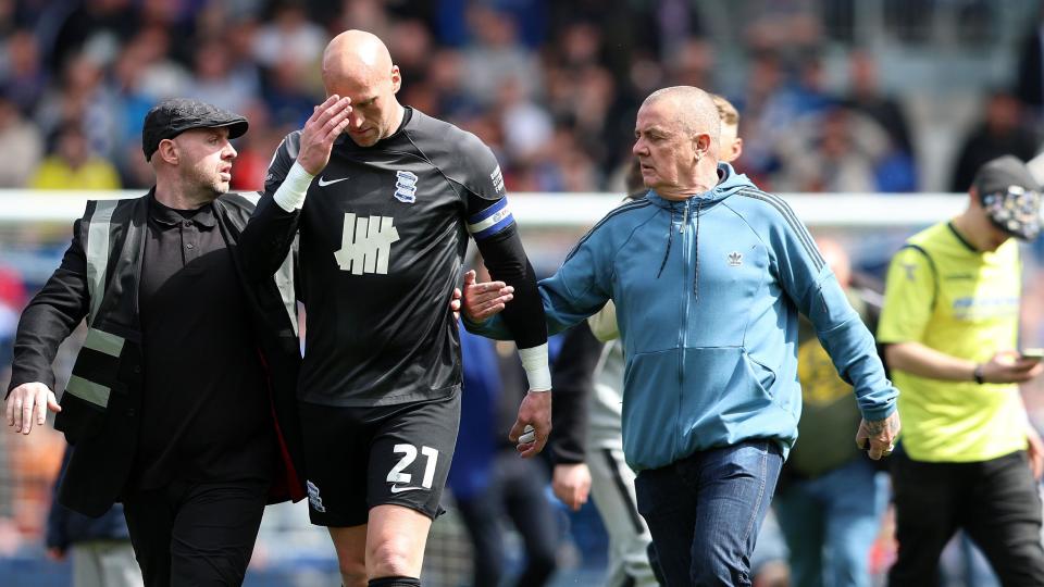 Goalkeeper John Ruddy puts his hand to his head while he is confronted by a fan on his left with a security guard to his right.