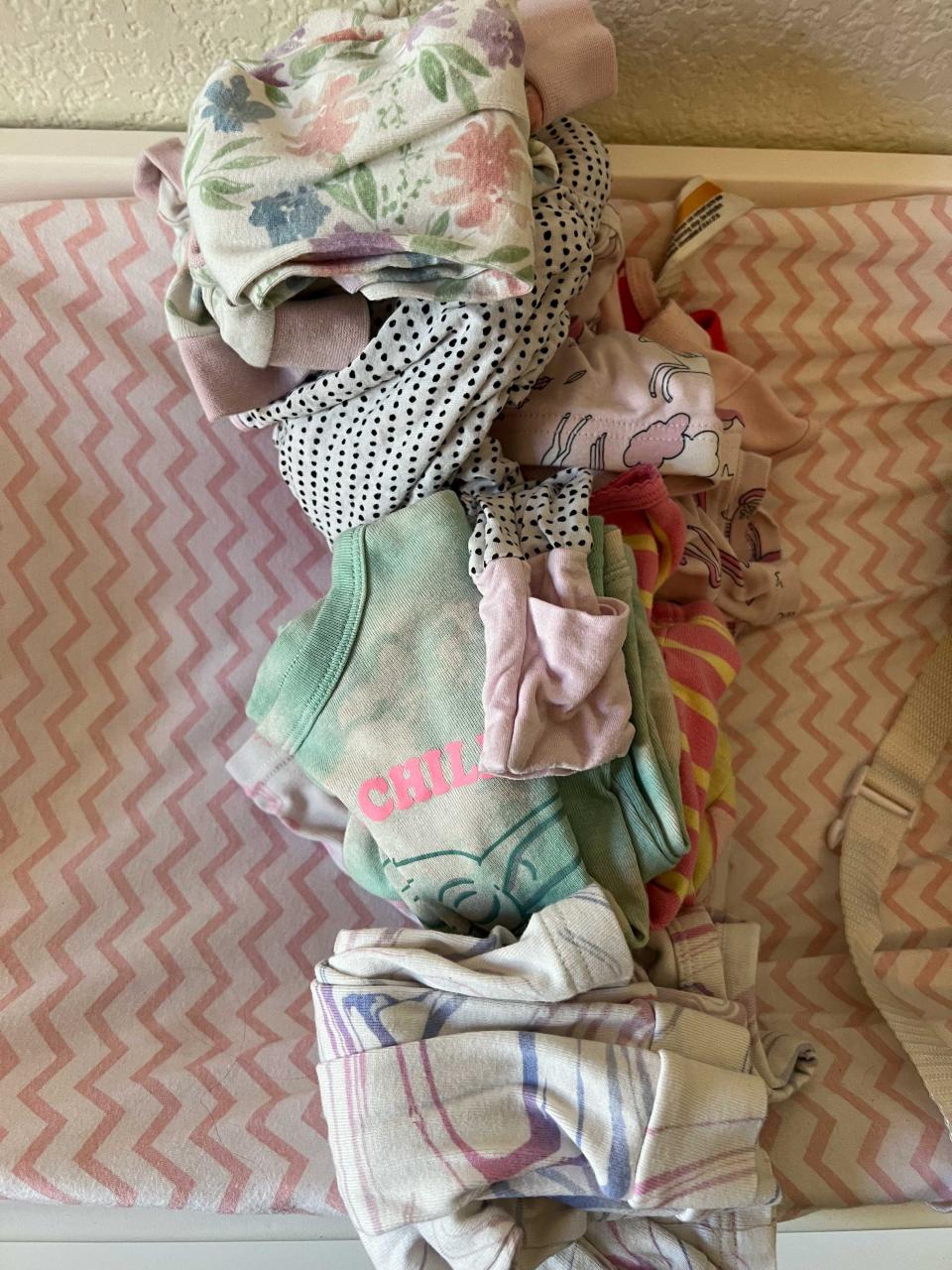 Three piles of children's clothes on a pink and white sheet.