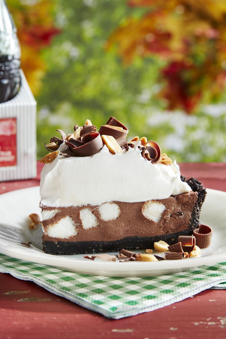 a slice of rocky road pie on a white plate with whipped cream and chocolate curls and chopped peanuts on top