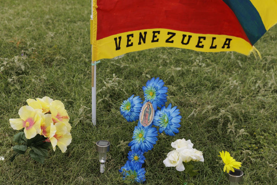 Flowers and a Venezuelan flag are displayed at a memorial site where eight migrants were killed, and several others injured the day before while waiting at a bus stop in Brownsville, Texas, Monday, May 8, 2023. (AP Photo/Michael Gonzalez)