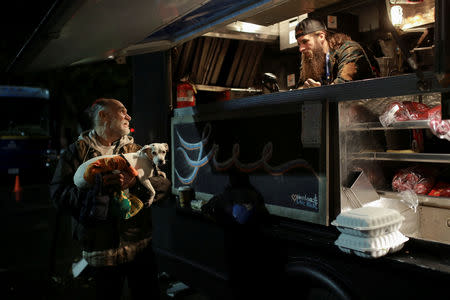 Bob Talk (L) who was in the process of moving out of the RV he rented in Paradise when the Camp Fire hit, holds his dog Princeton while talking to Kyle Pounders, who had just served him Thanksgiving dinner, in Chico, California, U.S. November 22, 2018. Pounders is a volunteer chef with World Central Kitchen and drove his food truck from Detroit to help out after hearing of the fire. REUTERS/Elijah Nouvelage