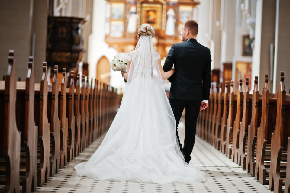 Rear shot of a stylish bride and father walk down the aisle of a grand catholic church.