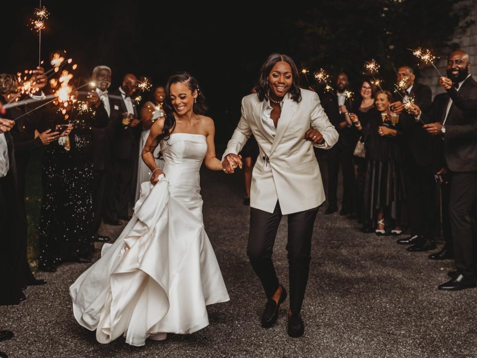 Two brides dance between their friends who hold sparklers.