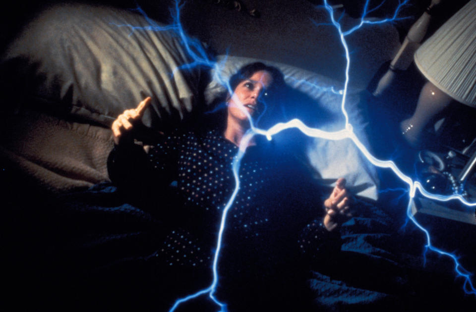 A young woman is amazed by a spontaneous electrical formation above her bed