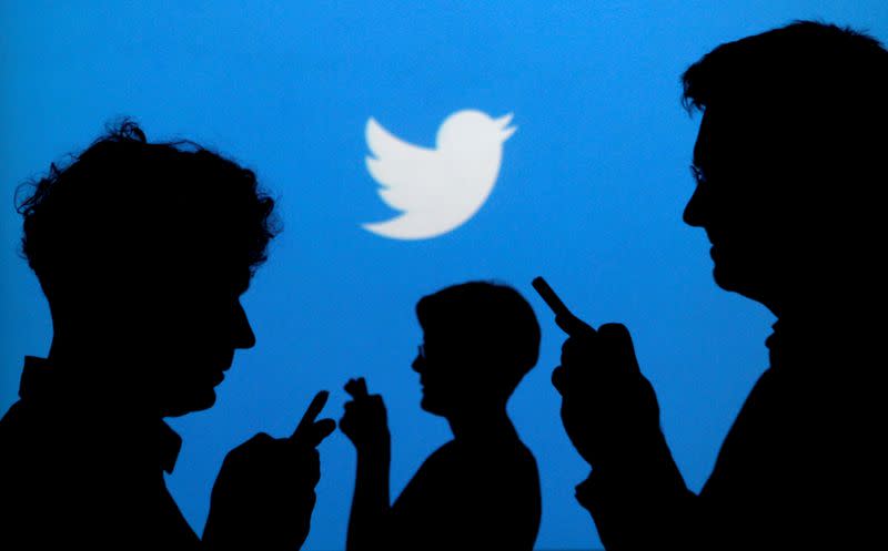 FILE PHOTO: People holding mobile phones are silhouetted against a backdrop projected with the Twitter logo