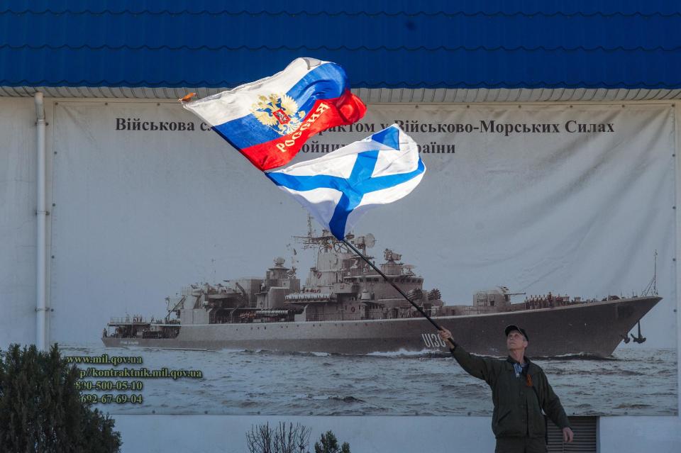 Un activista a favor de Rusia ondea las banderas del estado ruso y de la Armada rusa frente a la entrada de la Comandancia General de la Armada ucraniana en Sebastopol, Ucrania, el lunes 3 de marzo de 2014. (Foto AP/Andrew Lubimov)
