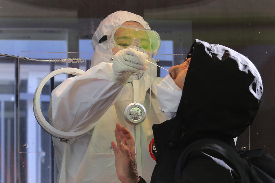 A medical worker in a booth takes a sample from a woman during COVID-19 testing at a makeshift clinic in Seoul, South Korea, Saturday, Jan. 2, 2021. South Korea is extending stringent distancing rules for two more weeks as authorities seek to suppress a viral resurgence, while confirming its first case of an apparently more contagious coronavirus variant detected in South Africa. (AP Photo/Ahn Young-joon)