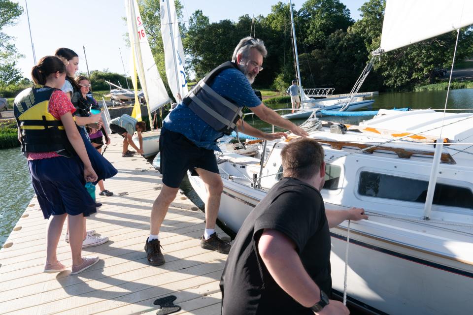 Shawnee Yacht Club commodore Jim Thompson, middle, helps Joshua Harsch, right, attach his pocket cruiser vessel, named Blue Heaven, to the dock to board participants at a recent exploring sailing lesson at Lake Shawnee.