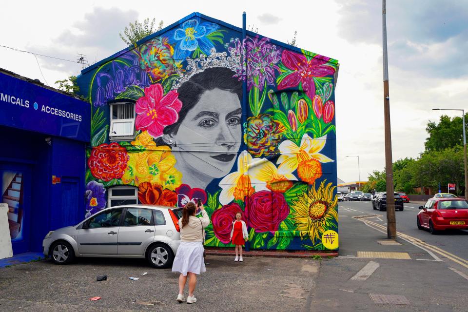 A young girl poses for a picture in front of a new mural of Queen Elizabeth II painted on a wall in Moreton, Wirral, on day one of the Platinum Jubilee celebrations (PA)