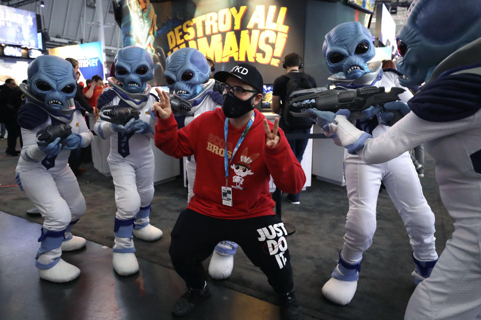 Eric Vita, of Morris Plains, N.J., center, wears a protective mask while posing for a photograph with people dressed as "Crypto," the main character in the video game "Destroy All Humans!," Thursday, Feb. 27, 2020, at the Pax East conference, in Boston. Vita said concerns about the coronavirus played a role in his decision to wear a mask to the conference. (AP Photo/Steven Senne)