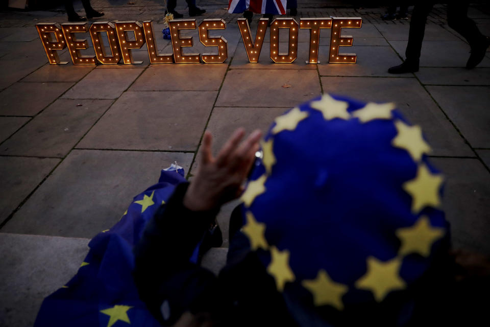 The lit up words "Peoples Vote", which calls for another referendum on Britain's European Union membership, are photographed by a remain, anti-Brexit supporter wearing a European flag design beret across the street from the Houses of Parliament in London, Monday, Dec. 10, 2018. British Prime Minister Theresa May has postponed Parliament's vote on her European Union divorce deal to avoid a shattering defeat — a decision that throws her Brexit plans into chaos. (AP Photo/Matt Dunham)