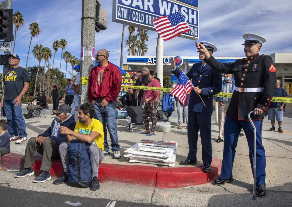 Men in military uniforms stand on a corner holding American flags