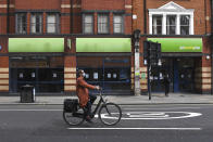 FILE - In this Thursday, April 30, 2020 file photo, a woman wearing a mask to protect against coronavirus, rides a bicycle past a job centre in Shepherd's Bush, as the lockdown to curb the spread of coronavirus continues, in London. The U.K. economy has officially fallen into a recession after official figures showed it contracting by a record 20.4% in the second quarter as a result of lockdown measures put in place to counter the coronavirus pandemic. The slump recorded by the Office for National Statistics follows a 2.2% quarterly contraction in the first three months of the year. (AP Photo/Alberto Pezzali, File)