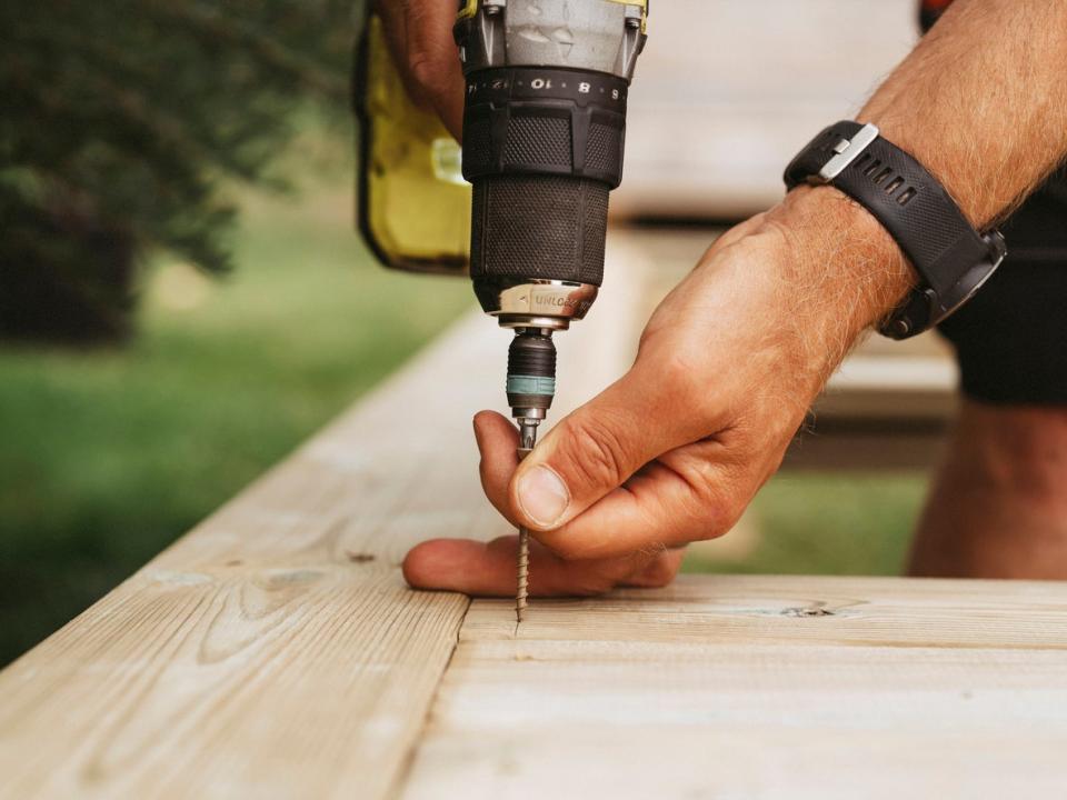 Screwdriver and man building a wooden patio deck outdoors in his garden