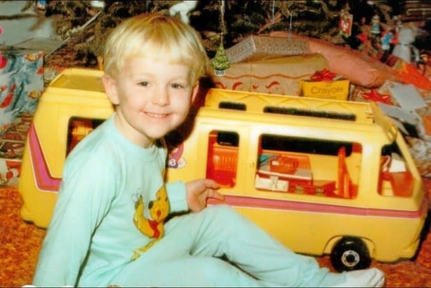 A young child in pajamas smiling and sitting in front of a toy camper