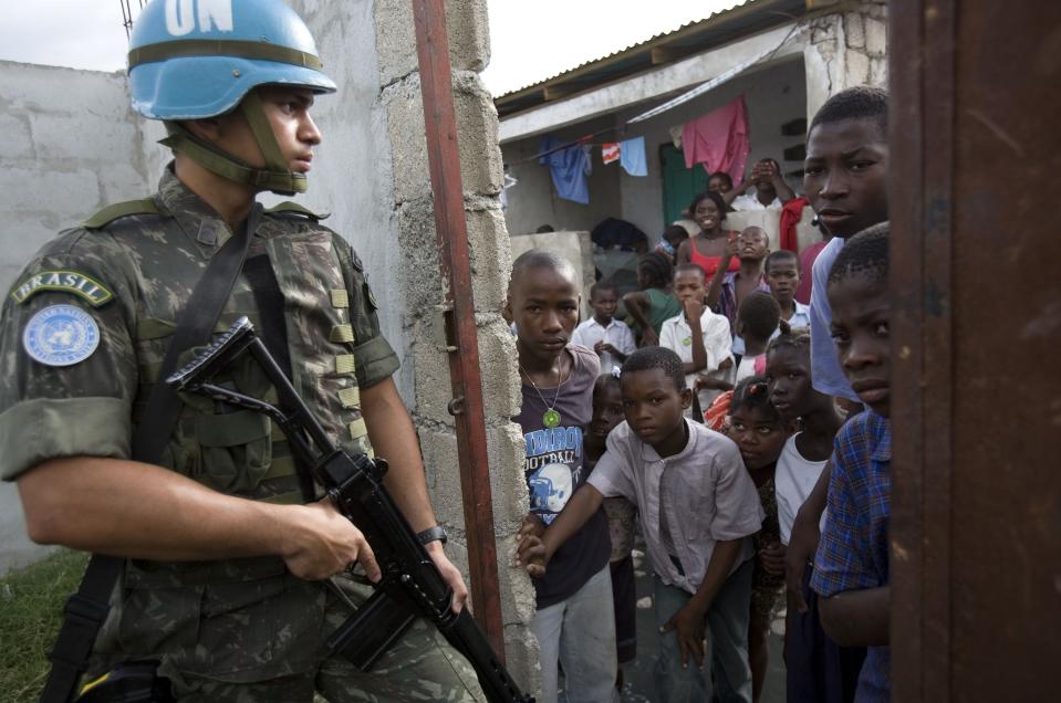 ARCHIVO - Un elemento de la misión de mantenimiento de paz de la ONU vigila mientras niños esperan afuera de una escuela en Puerto Príncipe, Haití, el martes 27 de mayo de 2008. (AP Foto/Ariana Cubillos, Archivo)