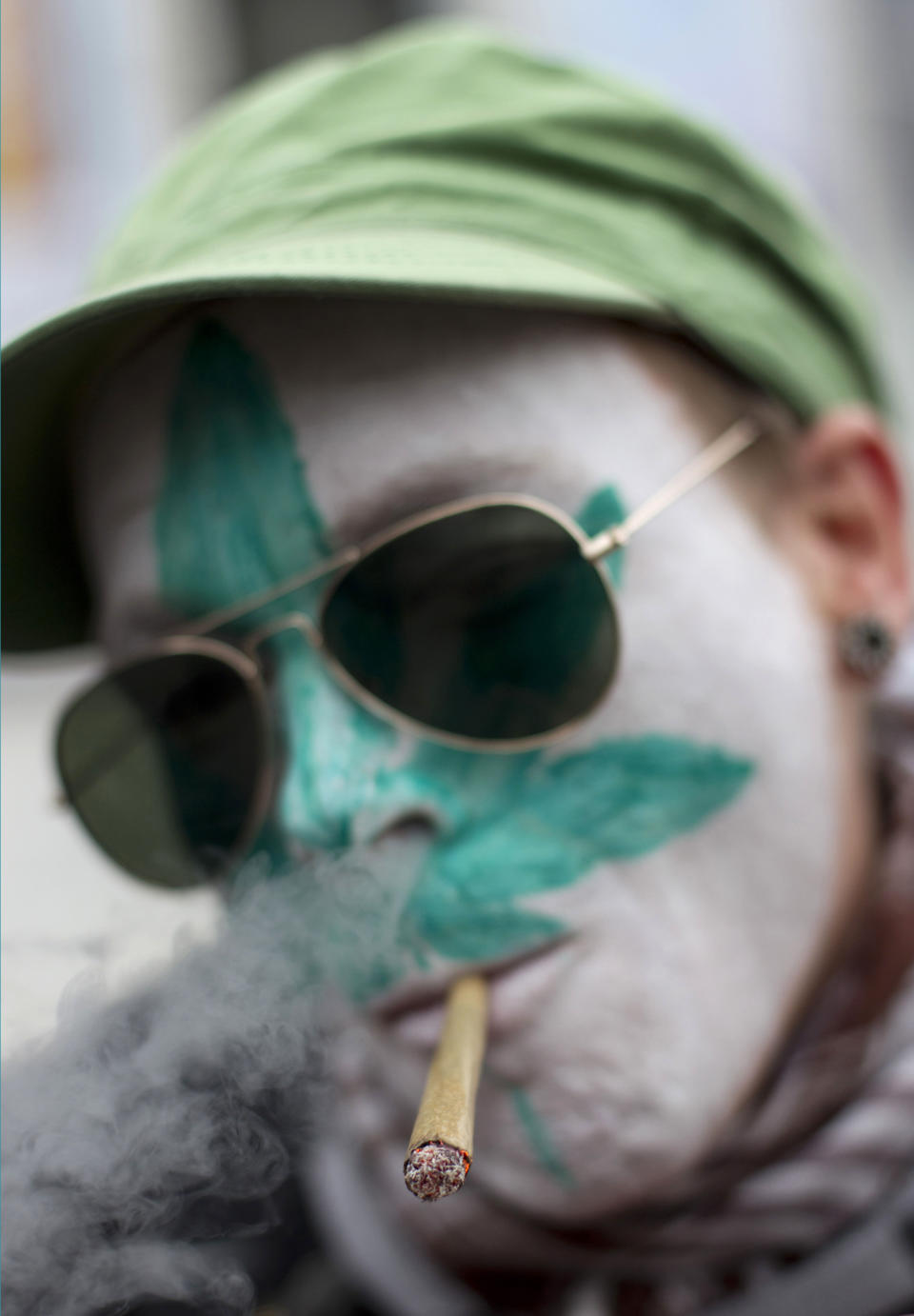 FILE - In this Friday April 20, 2012 file photo a protestor from Belgium with a marijuana leaf painted on his face smokes a marijuana joint in Amsterdam during a protest against a government plan to stop foreigners from buying marijuana in the Netherlands. The owners of three cannabis-selling cafes in Maastricht, southern Netherlands, went on trial Wednesday in the southern Netherlands charged with selling weed to foreigners, in a case both sides of a heated drugs debate in this border city hope will clarify the legality of a clampdown on so-called coffee shops. Maastricht is using new legislation banning coffee shops from selling cannabis and marijuana to people who don't live in the Netherlands as a way of clamping down on what the local mayor says was nuisance caused by hundreds of thousands of drug tourists driving into the picturesque heart of the city to stock up on weed. (AP Photo/Peter Dejong, File)