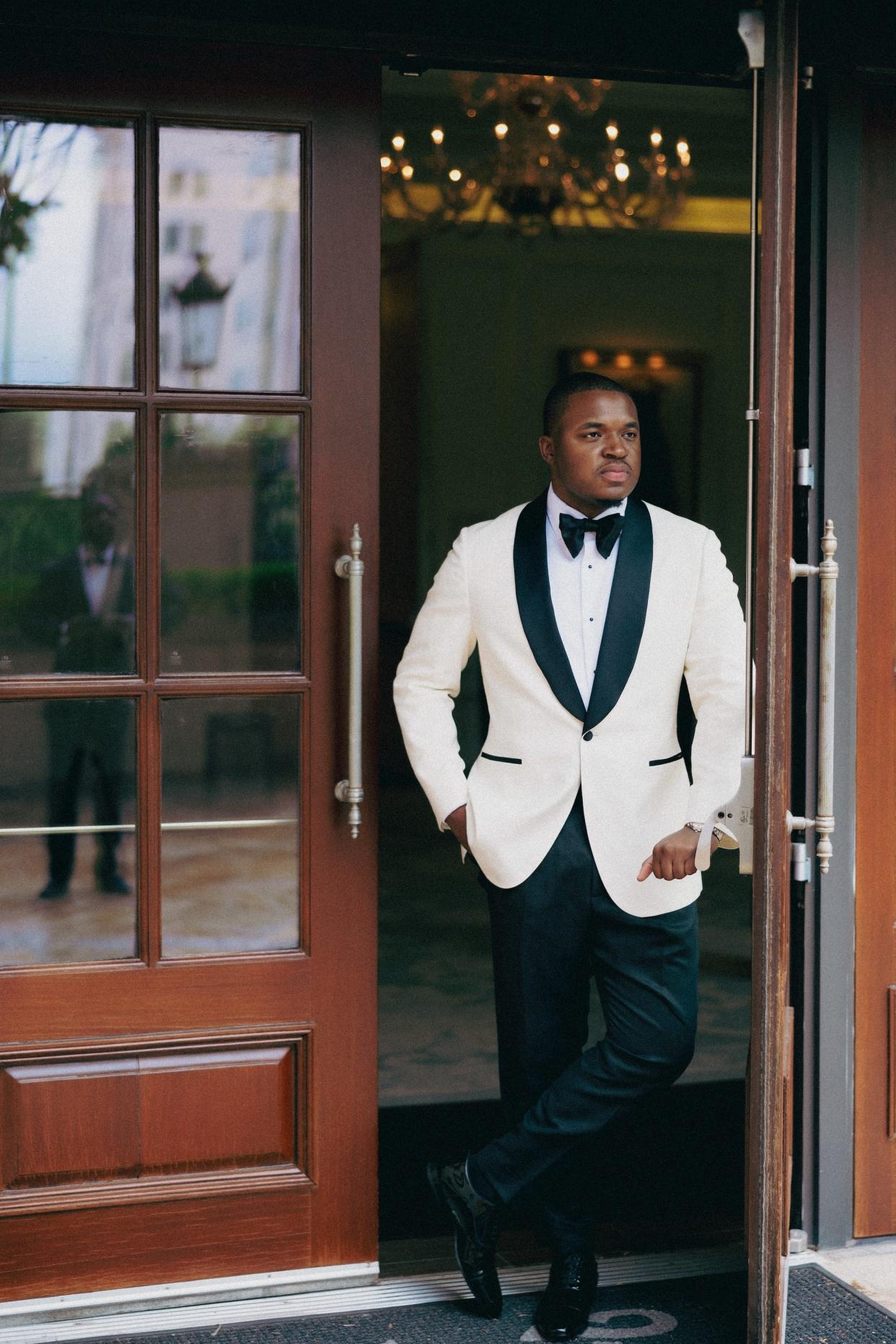 A man stands in a doorway in a white tuxedo jacket and black pants.