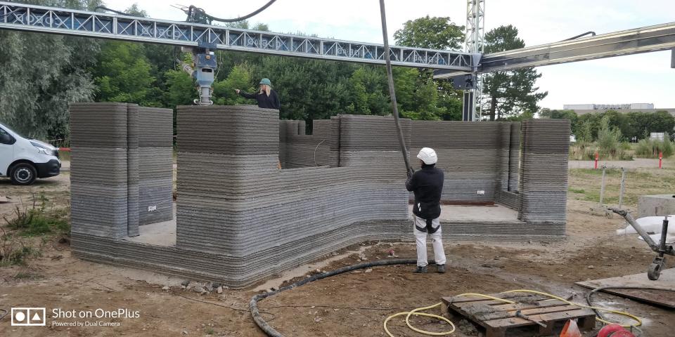 A person standing near 3D printed walls with a COBOD printer looming above.