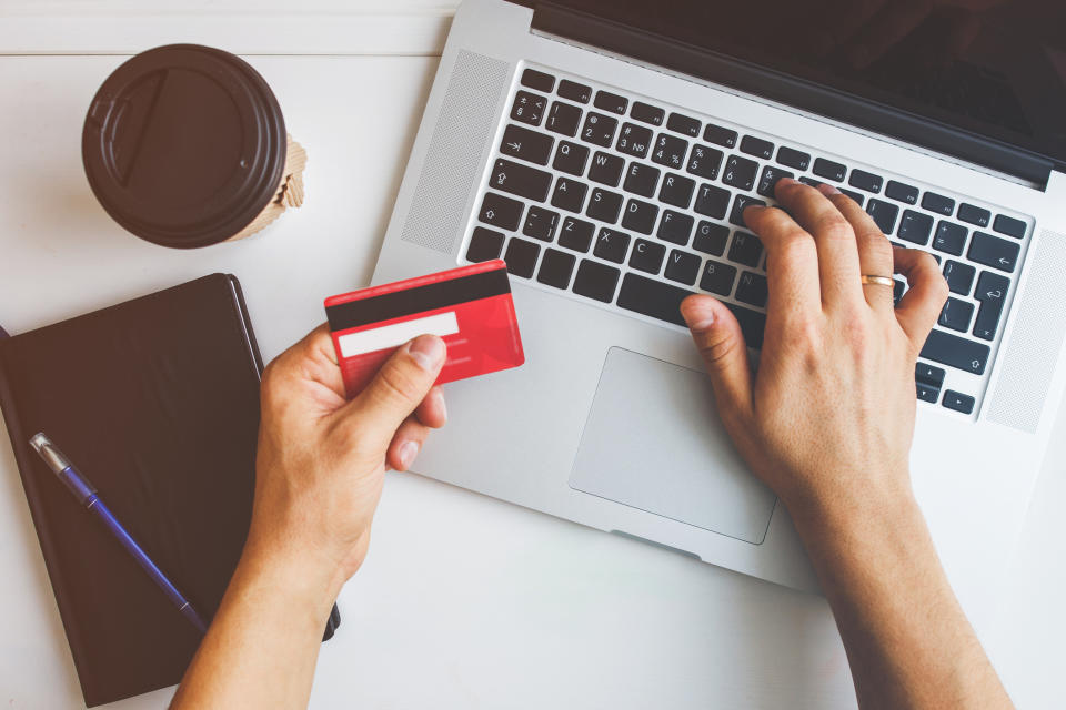 Person shopping online with credit card, laptop, notepad, and pen on desk for work and money article