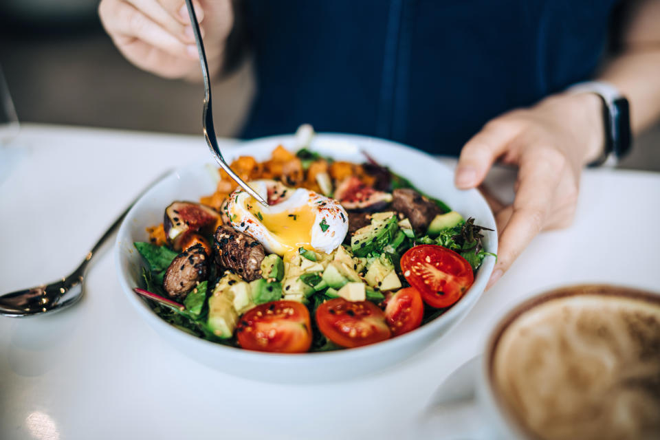 Close up shot of a woman eating a dish of fresh beef cobb salad with a soft boiled egg and coffee at a cafe table. Enjoying her healthy and nutritious lunch. Maintaining a healthy and well-balanced diet. The concept of healthy eating lifestyle