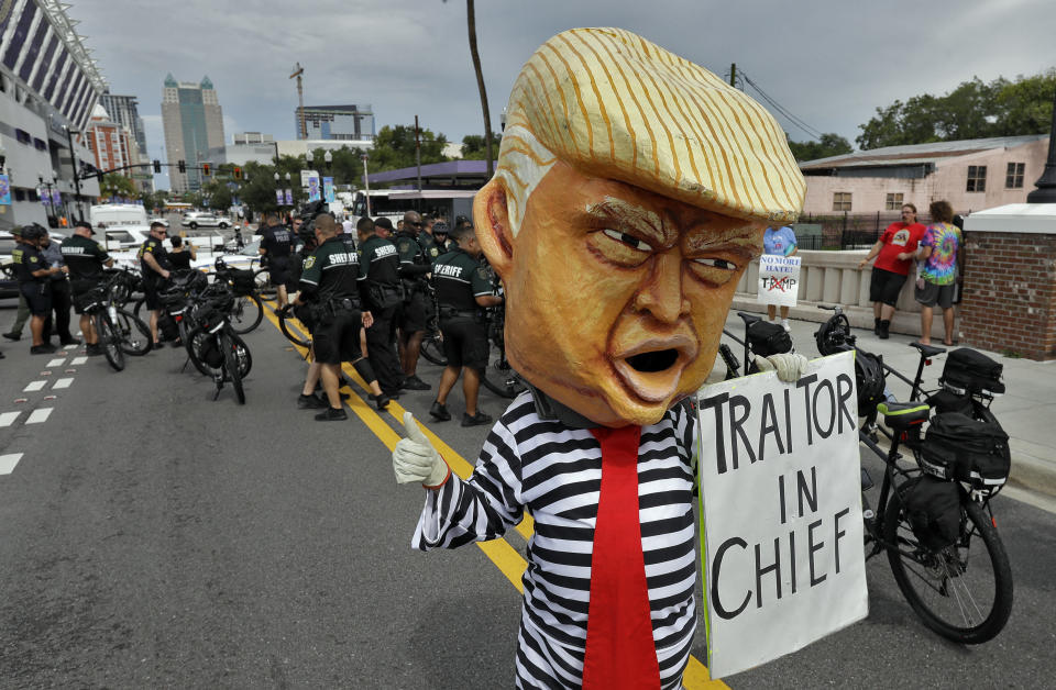 A protestor wearing a large President Donald Trump head walks near law enforcement officers during a rally Tuesday, June 18, 2019, in Orlando, Fla. A large of protestors were holding a rally near where Trump was announcing his re-election campaign. (AP Photo/Chris O'Meara)