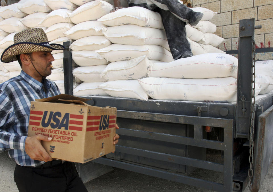 FILE - In this June 4, 2008 file photo, a Palestinian carries a box of vegetable oil as he walks past bags of flour, both donated by the United States Agency for International Development, at a depot in the West Bank village of Anin near Jenin. Tens of thousands of Palestinians are no longer getting food aid or health services from America after the Trump administration’s decision in 2018 to cut more than $200 million in aid to the Palestinians. Before the aid cuts were announced, it provided food aid -- branded as a gift from the American people -- to more than 180,000 Palestinians in the Israeli-occupied West Bank and Gaza on behalf of the World Food Program. (AP Photo/Mohammed Ballas, File)