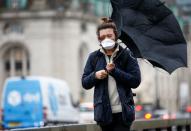 A man wearing a protective face mask walks with an umbrella in London