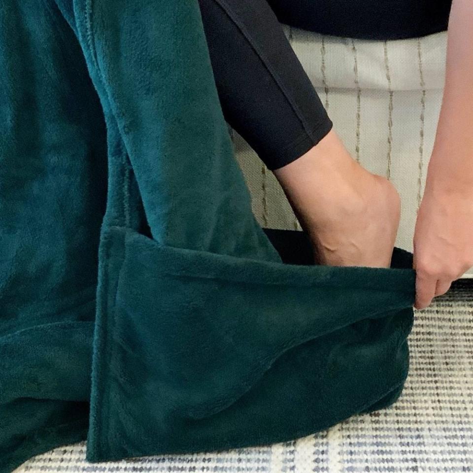 A person is seated, trying on soft, plush green slippers on a white patterned rug