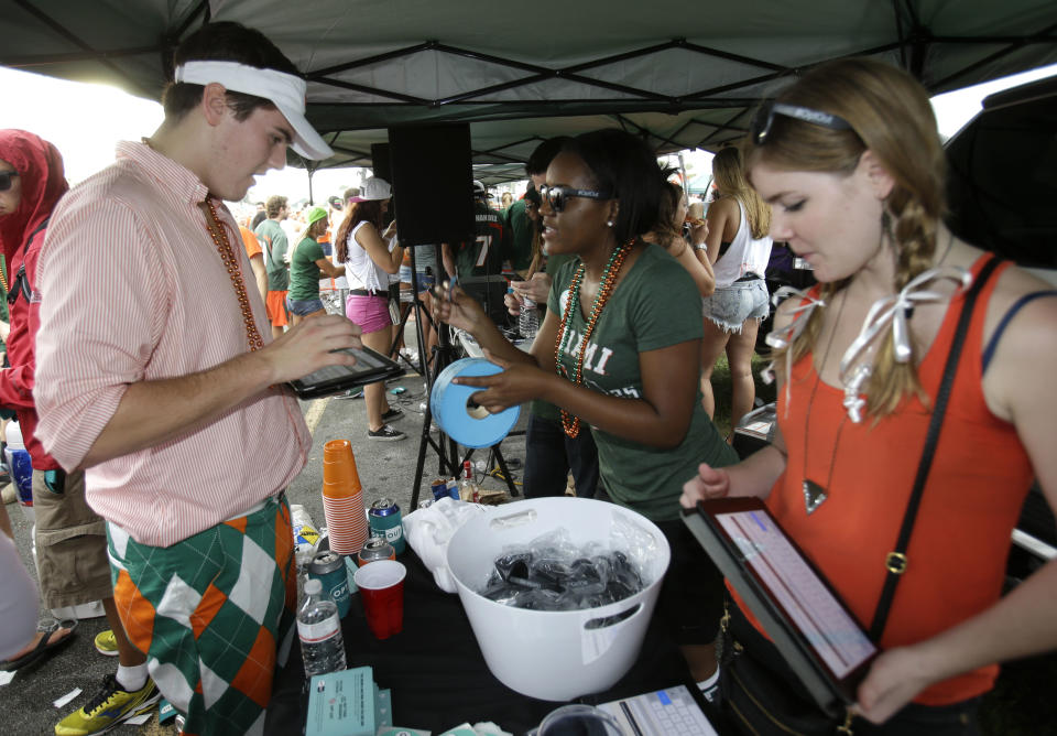 In this Saturday, Nov. 9, 2013 photo, Miami student Mack Sokul, 18, left, fills out a survey at a tent set up by Generation Opportunity, a national conservative organization that targets young adults, while tailgating before the start of an NCAA college football game between Miami and Virginia Tech, in Miami Gardens, Fla. It may be the hottest tailgate party at the University of Miami's homecoming game, but the 100-yard stretch of free pizza and party tents, is also a carefully crafted strategy aimed at getting students to opt out of President Barack Obama's controversial new health law. (AP Photo/Wilfredo Lee)