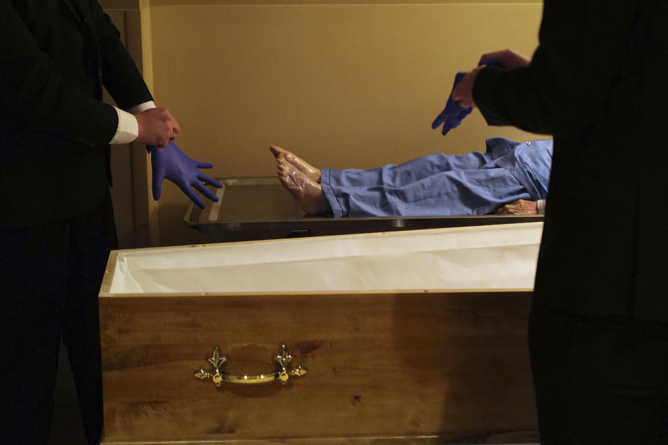 Pallbearers, Louis Mercier, right, and Allan Pottier, left, prepare to carry the body of a 105-year-old woman as they prepare her for funeral at a mortuary, in Paris, Friday, April 24, 2020, as a nationwide confinement continues to counter the COVID-19 virus. As body after body has passed through his rubber-gloved hands, sealed in double-layered bags for disposal, Paris undertaker Franck Vasseur has become increasingly concerned about the future after the coronavirus pandemic. All these people ferried in his hearse to cremations that their loved ones couldn't attend: when will they be mourned? (AP Photo/Francois Mori)