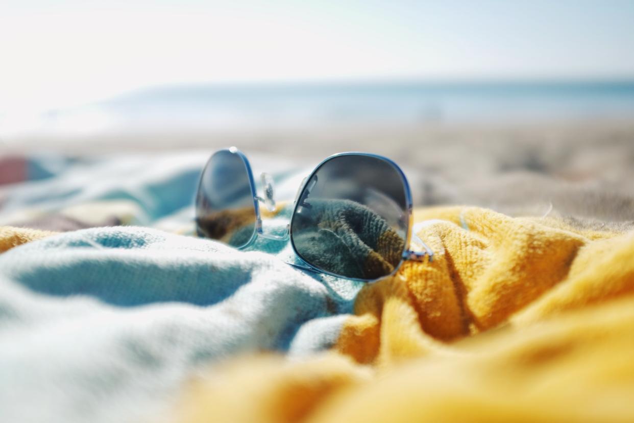 Sunglasses laying on colourful beach towel on sandy beach in summer