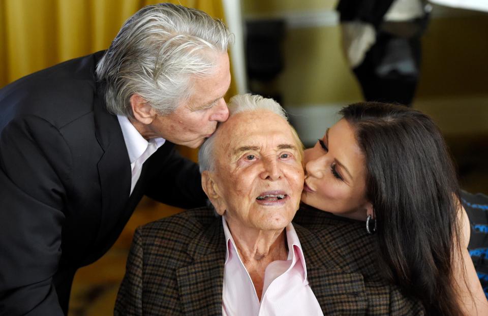 Kirk Douglas (center) gets a kiss from his son Michael Douglas and Michael's wife Catherine Zeta-Jones during his 100th birthday party.