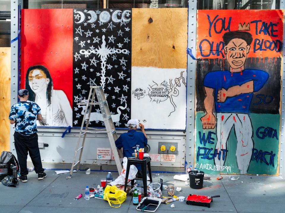 Artists paint on the boarded-up windows of a building in SoHo on June 20, 2020 in New York City.
