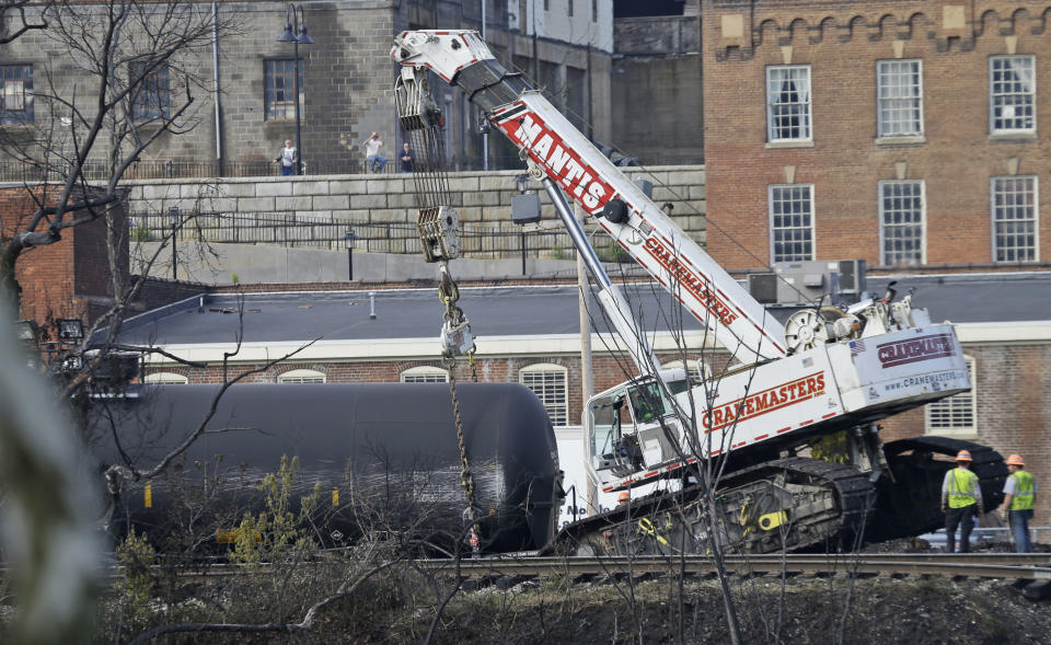 Workers remove damaged tanker cars along the tracks where several CSX tanker cars carrying crude oil derailed and caught fire along the James River near downtown Lynchburg, Va., Thursday, May 1, 2014. Virginia state officials were still trying Thursday to determine the environmental impact of the train derailment. (AP Photo/Steve Helber)