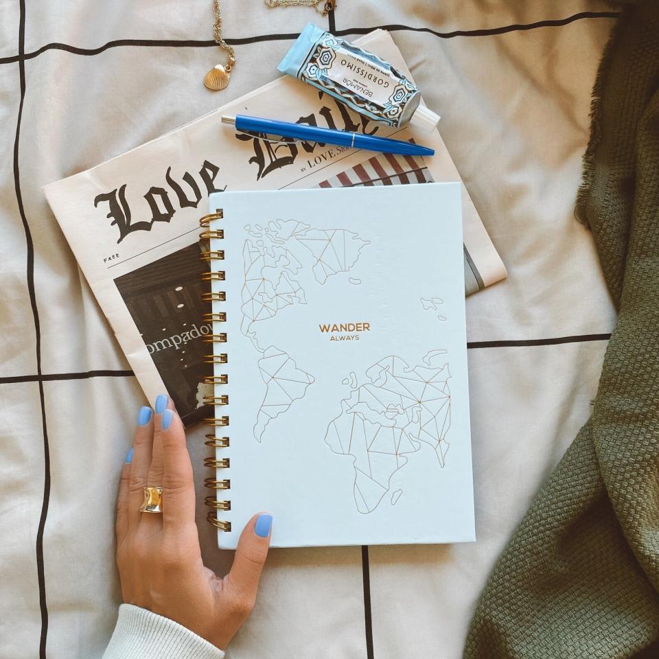 Model holding spiral notebook with minimalist gold map that says "Wander Always"